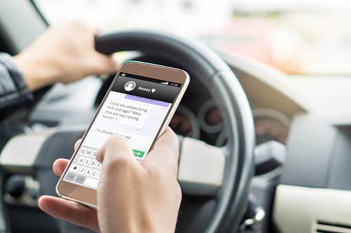 driver texting with a cellphone in one hand while he drives with the other, putting everyone at risk of a car accident.