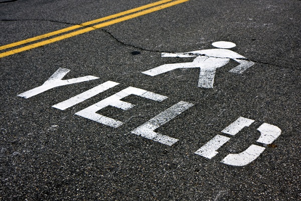 A white painted road marking on dark asphalt that reads "YIELD" next to a pedestrian walking icon.